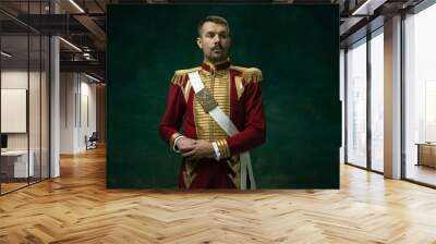 Highly serious. Young man in suit as Nicholas II isolated on dark green background. Retro style, comparison of eras concept. Beautiful male model like historical character, monarch, old-fashioned. Wall mural