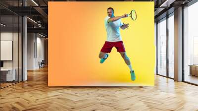 In jump. One caucasian man playing tennis on studio background in neon light. Fit young professional male player in motion or action during sport game. Concept of movement, sport, healthy lifestyle. Wall mural