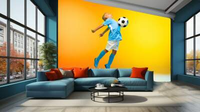 In jump. Young boy as a soccer or football player in sportwear practicing on gradient yellow studio background in neon light. Fit playing boy in action, movement, motion at game. Copyspace. Wall mural