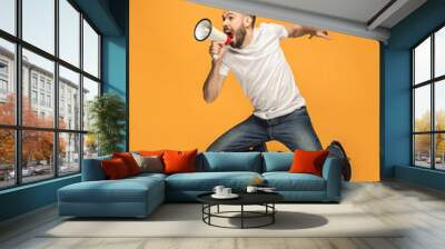 Jumping fan on orange background. The young man as soccer football fan with megaphone Wall mural