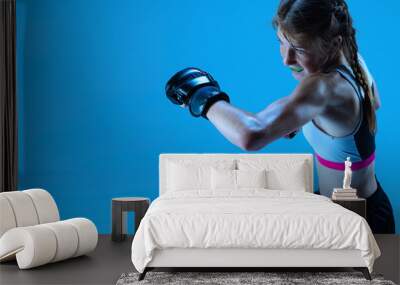 Junior league. Young girl MMA fighter practicing punch isolated on blue background in neon light. Concept of sport, competition, action, achievements Wall mural