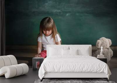 Little girl with teddy bear sitting on floor in empty room. Autism concept Wall mural