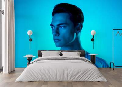 Look. Handsome caucasian man's portrait isolated on blue studio background in neon, monochrome. Beautiful male model. Concept of human emotions, facial expression, sales, ad, fashion and beauty. Wall mural