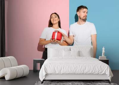 Love. Giving a gift for St. Valentines Day. Young man and woman in casual clothes on pink, blue bicolored background. Concept of human emotions, facial expession, relations, ad. Beautiful couple. Wall mural