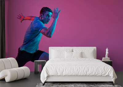 One Caucasian professional male athlete, runner training isolated on pink studio background with blue neon filter, light. Muscular, sportive man. Flyer Wall mural