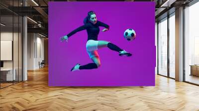 One sportive girl, female soccer player kick in jump football ball isolated on purple studio background in neon light. Sport, action, motion, fitness Wall mural