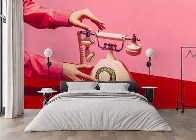 Pop art photography. Retro objects, gadgets. Female hand holding handset of vintage phone isolated on pink and red background. Vintage, retro fashion style Wall mural