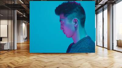 Portrait of a guy with colorful neon light on blue studio background. Male model with calm and serious mood. Facial expression, cyberpunk, millenials lifestyle and look like. Future, technologies. Wall mural