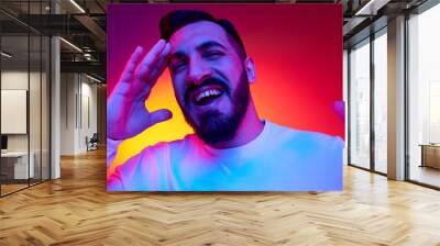 Portrait of bearded handsome man cheerfully smiling against gradient multicolored studio background in neon light. Happiness, positive vibe. Concept of human emotions, facial expression, lifestyle Wall mural