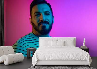 Portrait of handsome mature bearded man in striped shirt looking at camera with tender smile against gradient studio background in neon light. Concept of human emotions, facial expression, lifestyle Wall mural