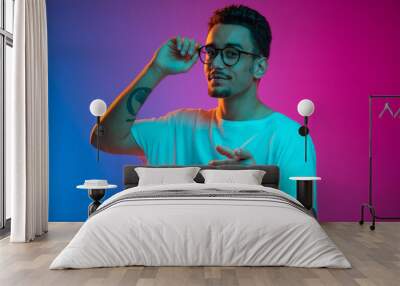 Portrait of Latina young man posing isolated on gradient purple pink background in neon light. Front view Wall mural