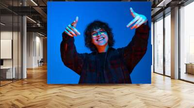 Portrait of young cheerful boy, student in black shirt isolated on dark blue background in neon light. Concept of emotions, facial expression, youth, aspiration, sales Wall mural