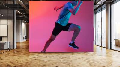 Portrat of Caucasian professional male athlete, runner training isolated on pink studio background with blue neon filter, light. Muscular, sportive man. Wall mural