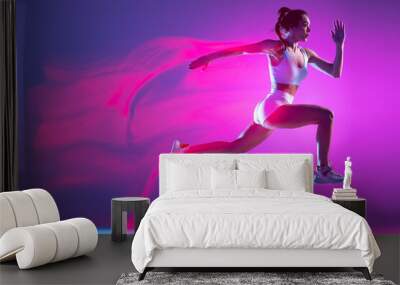 Professional female athlete, runner training isolated on blue studio background in mixed pink neon light. Healthy lifestyle, sport, motion and action concept. Wall mural