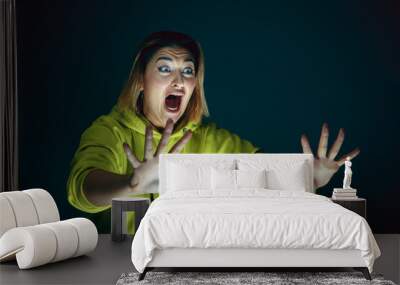 Screaming. Portrait of young crazy scared and shocked caucasian woman isolated on dark background. Copyspace for ad. Bright facial expression, human emotions concept. Looking horror on TV, cinema. Wall mural