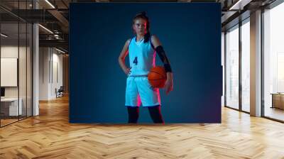 Self-building. Young caucasian female basketball player on blue studio background in neon light, motion and action. Concept of sport, movement, energy and dynamic, healthy lifestyle. Posing confident. Wall mural