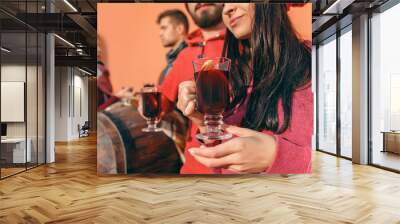 Smiling european men and women during party photoshoot. The guys posing as friends at studio fest with wineglasses with hot mulled wine on foreground. Wall mural