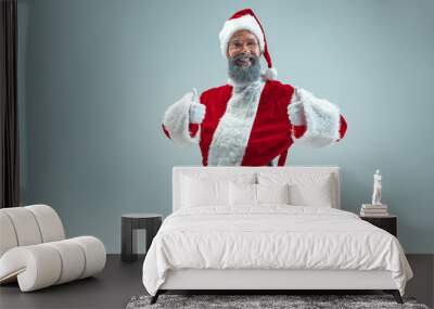 Smiling funny guy with christmas hat posing at studio with sign ok. New Year Holiday. Christmas, x-mas, winter, gifts concept. Man wearing Santa Claus costume on gray. Copy space. Winter sales. Wall mural