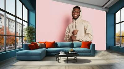 Smiling guy, young dark skinned man wearing hoodie, youth clothes isolated on pink studio background with copyspace for ad. Wall mural