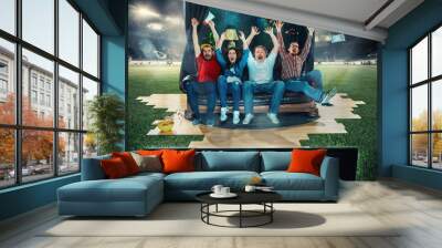 Soccer football fans sitting on the sofa and watching TV in the middle of a football field. Wall mural