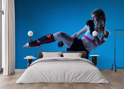 Studio shot of sportive teen-girl, MMA fighter in action, motion isolated on blue background in neon light. Concept of sport, competition, action, achievements Wall mural