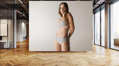 Studio shot of young charming slim girl in grey cotton underwear isolated over gray background. Wellness, fitness, diet, fashion, natural beauty of female body Wall mural