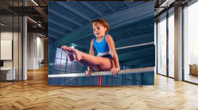 The beautiful little girl is engaged in sports gymnastics on a parallel bars at gym. The performance, sport, acrobat, acrobatic, exercise, training concept Wall mural