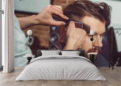 The hands of young barber making haircut to attractive man in barbershop Wall mural