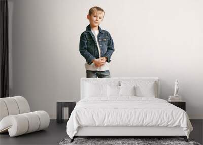 the portrait of cute little kid boy in stylish jeans clothes looking at camera against white studio  Wall mural