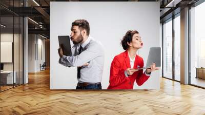 The young businessman and businesswoman with laptops kissing screens on gray background Wall mural