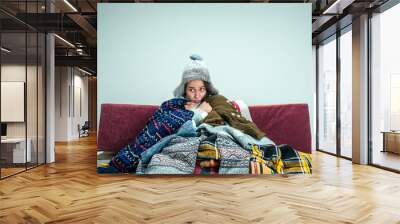 The young sick woman with flue sitting on sofa at home or studio covered with knitted warm clothes. Illness, influenza, pain concept. Relaxation at Home. Healthcare Concepts. Wall mural