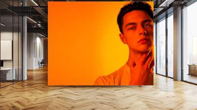 Thoughtful. Handsome caucasian man's portrait isolated on orange studio background in neon, monochrome. Beautiful male model. Concept of human emotions, facial expression, sales, ad, fashion beauty Wall mural