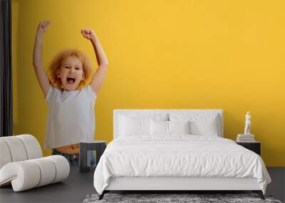 Thrilled little girl, kid shouting in rejoice and raising hands up isolated over yellow background. Concept of children positive emotions Wall mural