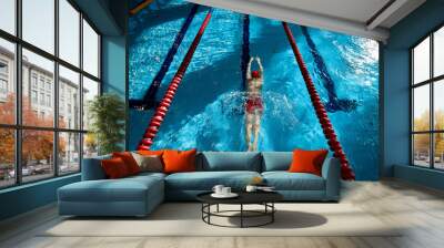 Top view of muscular, athletic young man, swimmer in red cap in motion, showing strength, training, swimming in pool indoors. Concept of professional sport, health, endurance, active lifestyle Wall mural