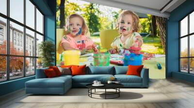 Two-year old girls painting with poster paintings together against green lawn Wall mural