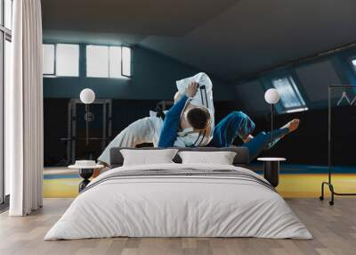 Two young judo caucasian fighters in white and blue kimono with black belts training martial arts in the gym with expression, in action, motion. Practicing fighting skills. Overcoming, reaching target Wall mural