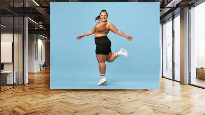 Young, happy, active, overweight woman training in sportswear against blue studio background. Self-love and acceptance. Concept of sport, body-positivity, weight loss, body and health care Wall mural