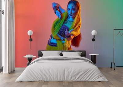 Young beautiful woman in traditional indian dress and makeup dancing against gradient studio background in neon light. Concept of beauty, fashion, India, traditions, lifestyle, choreography, art. Ad Wall mural