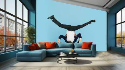 Young caucasian businessman having fun dancing break dance on blue studio background. Management, flexible, freedom, professional occupation, alternative way of modern working. Loves his job Wall mural