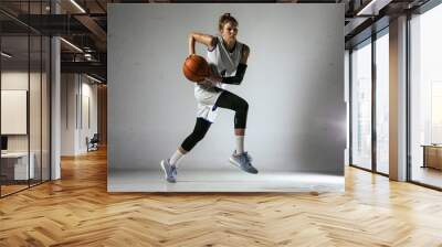 Young caucasian female basketball player of team in action, motion in jump isolated on white wall background. Concept of sport, movement, energy and dynamic, healthy lifestyle. Training, practicing. Wall mural