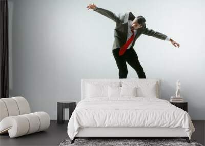 Young caucasian man moving flexible on white studio background. Male model in office attire bending over, avoiding something, catched in motion and action. Looks angry, scared, fighting. Emotions. Wall mural