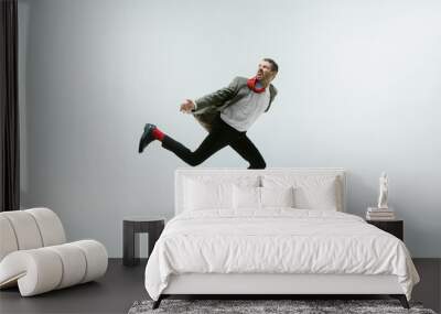 Young caucasian man moving flexible on white studio background. Male model in office attire bending over, avoiding something, catched in motion and action. Looks angry, scared, fighting. Emotions. Wall mural