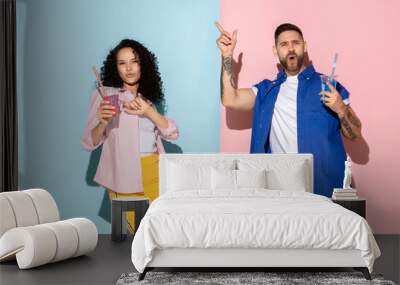 Young emotional caucasian couple in bright casual clothes posing on pink and blue background. Concept of human emotions, facial expession, relations, ad. Man and woman going to drink cocktails. Wall mural