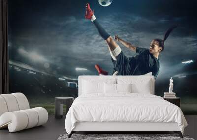 Young female soccer or football player with long hair in sportwear and boots kicking ball for the goal in jump at the stadium. Concept of healthy lifestyle, professional sport, hobby, motion, movement Wall mural