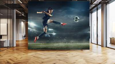 Young female soccer or football player with long hair in sportwear and boots kicking ball for the goal in jump at the stadium. Concept of healthy lifestyle, professional sport, hobby, motion, movement Wall mural