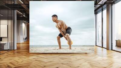 Young healthy man athlete doing exercise with the weight at the beach. Signle male model shirtless training at the river side in sunny day. Concept of healthy lifestyle, sport, fitness, bodybuilding. Wall mural