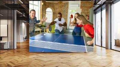 Young people playing table tennis in workplace, having fun. Friends in casual clothes play ping pong together at sunny day. Concept of leisure activity, sport, friendship, teambuilding, teamwork. Wall mural