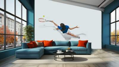 Young woman in blue shirt playing tennis. She hits the ball with a racket. Indoor studio shot isolated on white. Youth, flexibility, power and energy. Negative space. Top view. Wall mural