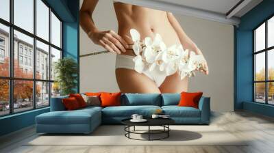 Young woman with epilated bikini zone holding flower isolated on gray studio background. Cut out part of body. Medical problem and solution. Wall mural