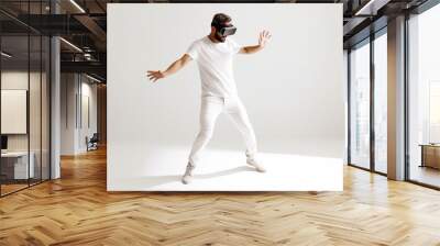 Young man wearing virtual reality goggles, standing on white studio background. Wall mural